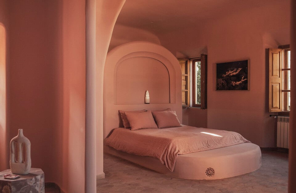 Hotel Corazón, Balearic Islands, Spain — Terracotta bedroom with arched alcove, curved platform bed, warm natural light, minimalist design, Mediterranean architecture.