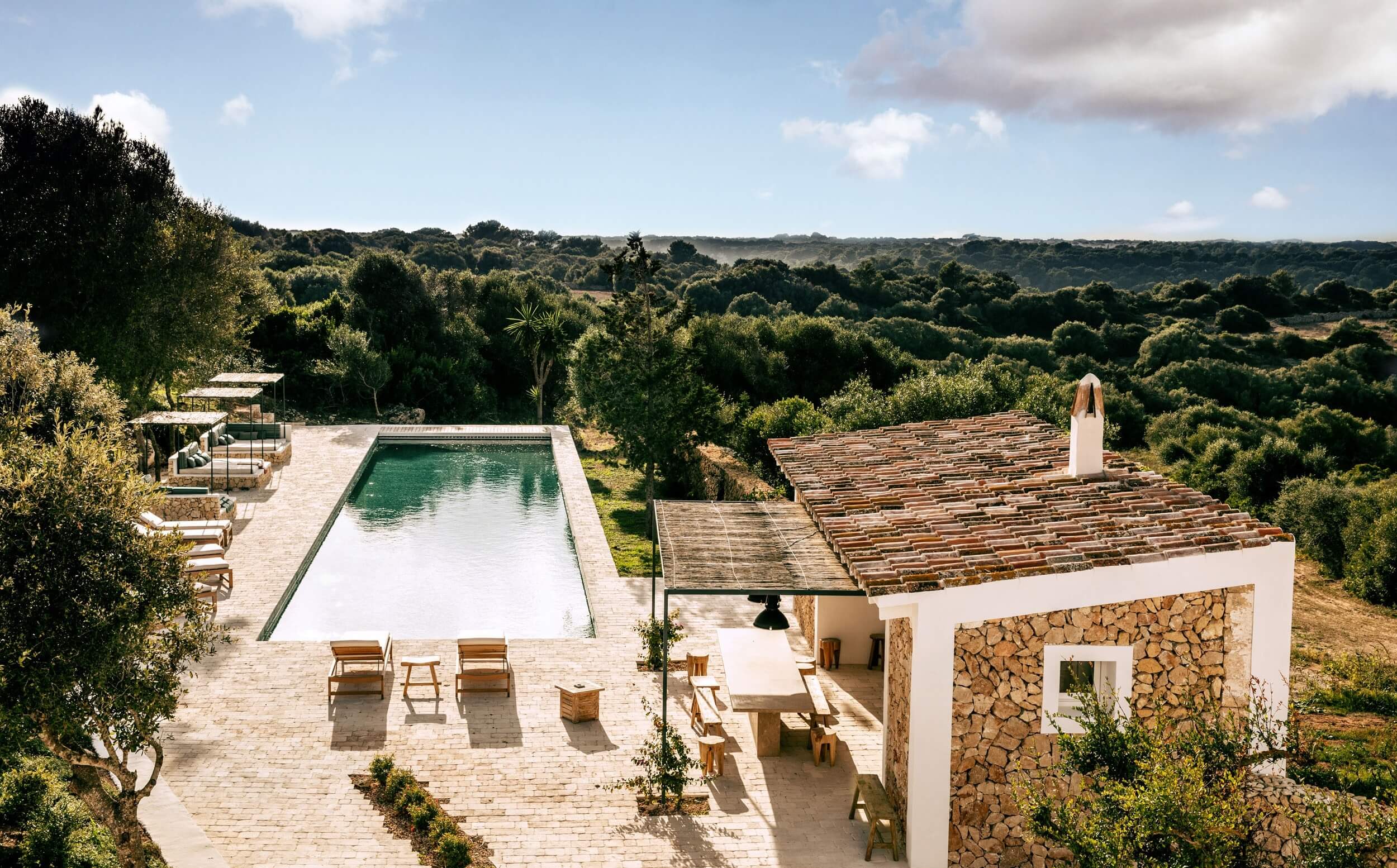 Es Bec d’Aguila — Es Bec d'Aguila, Balearic Islands, Spain — Minimalist villa with infinity pool overlooking forested landscape, stone and white architecture, wooden lounge chairs, afternoon light.
