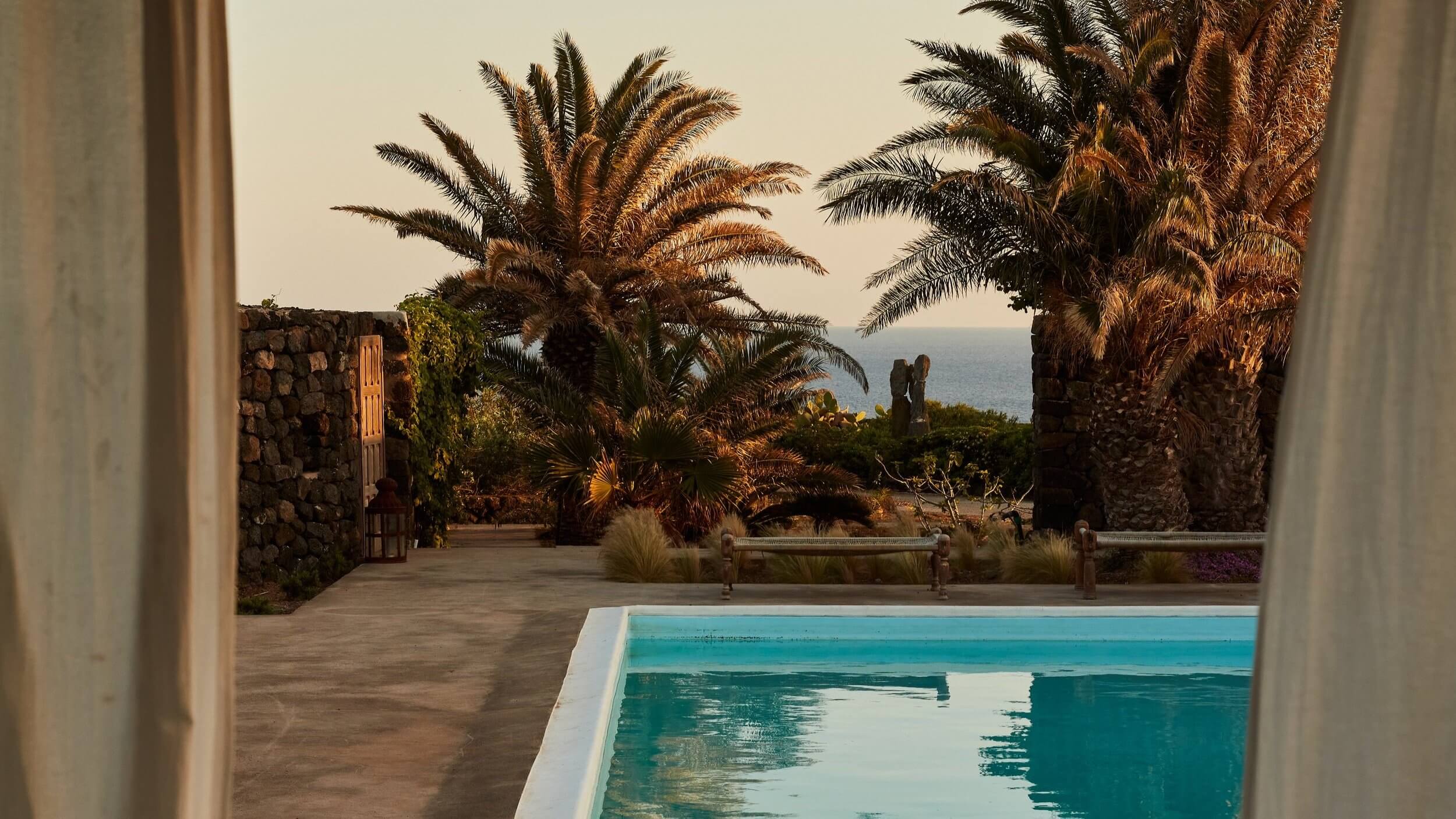 Parco Dei Sesi, Europe — Turquoise pool edge framing palm-lined courtyard with sea view, stone architecture, Mediterranean coastal setting.