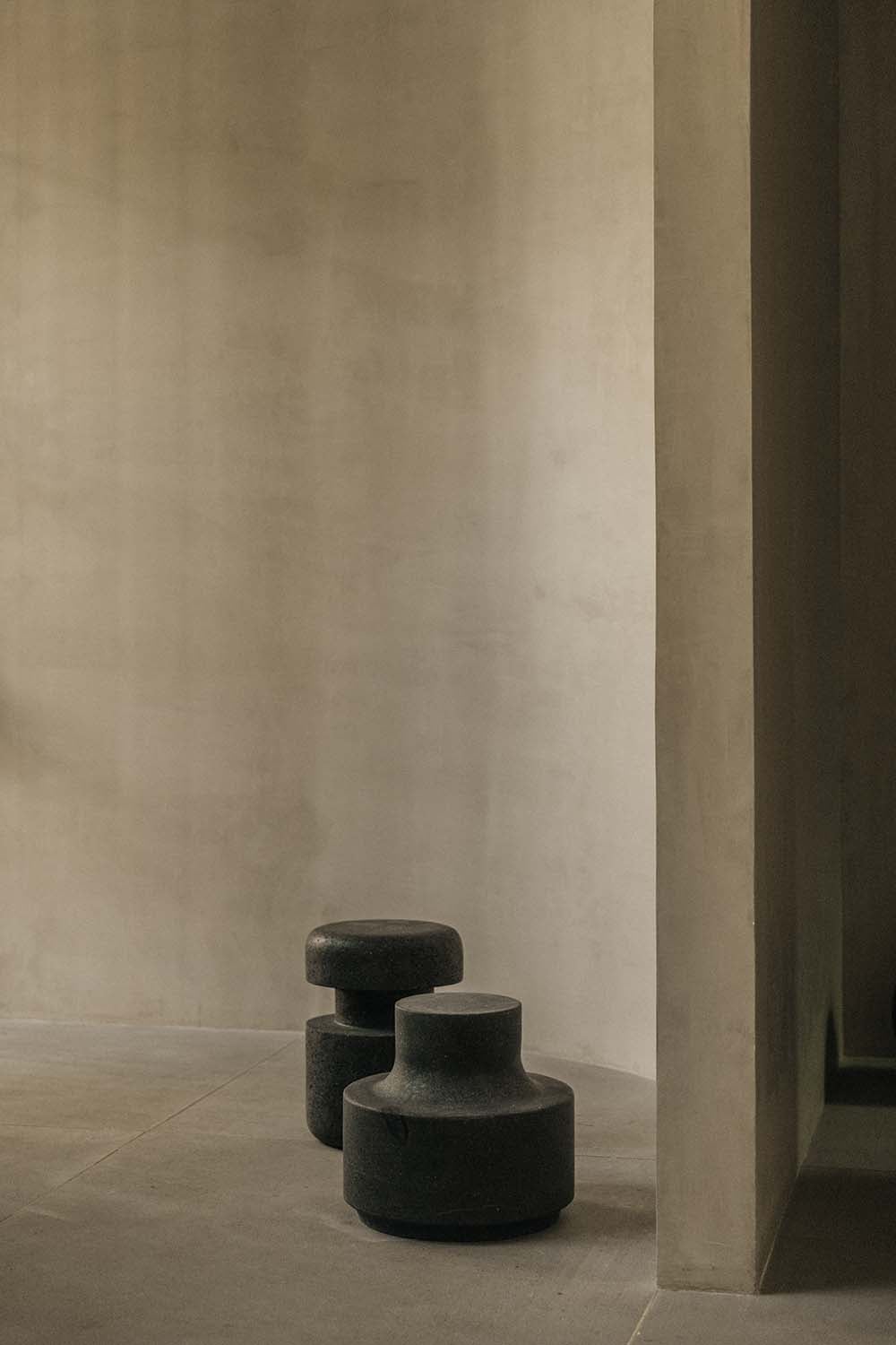 Octavia Casa, Mexico — Dark stone sculptural stools in minimalist white gallery space with concrete flooring and soft natural light.