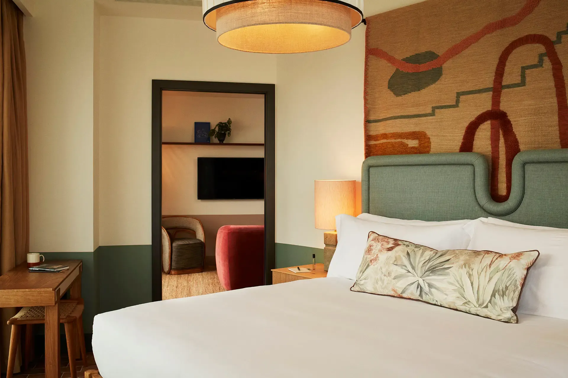 The Hoxton Poblenou, Barcelona, Spain — Modernist bedroom with sage headboard, terracotta abstract wall art, warm pendant lighting, and mid-century furnishings.
