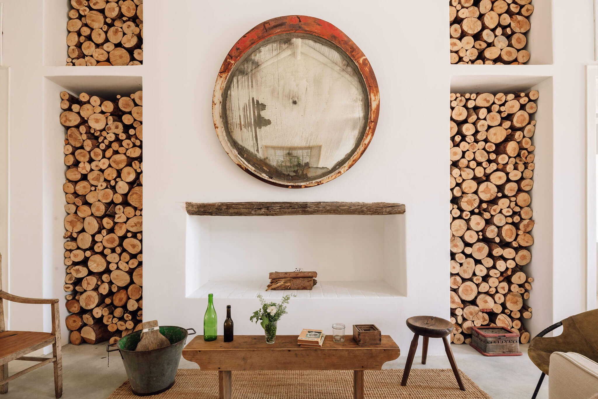 Hospedaria, Europe — Minimalist interior with stacked wood-slice wall installations, rustic mirror, wooden table, and natural light creating warm, curated aesthetic.