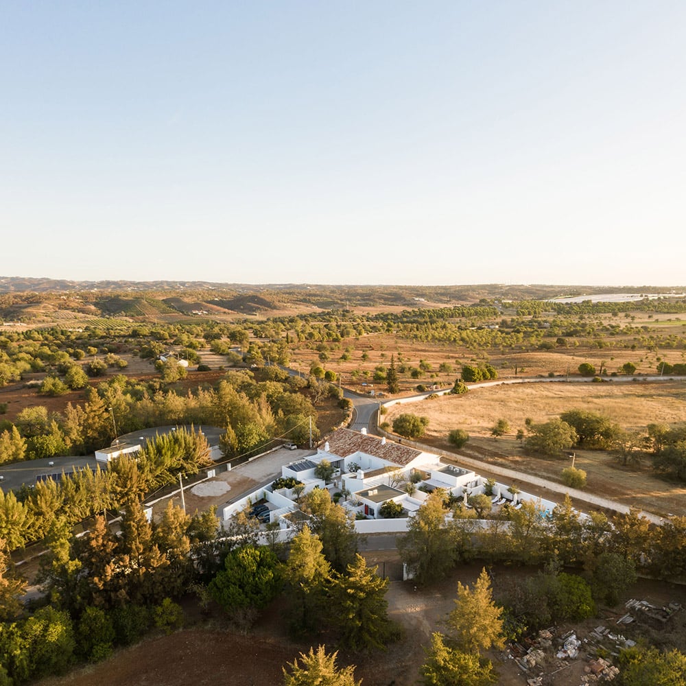 Hospedaria, Europe — Aerial view of whitewashed modernist villa nestled among pine trees overlooking river valley at golden hour.