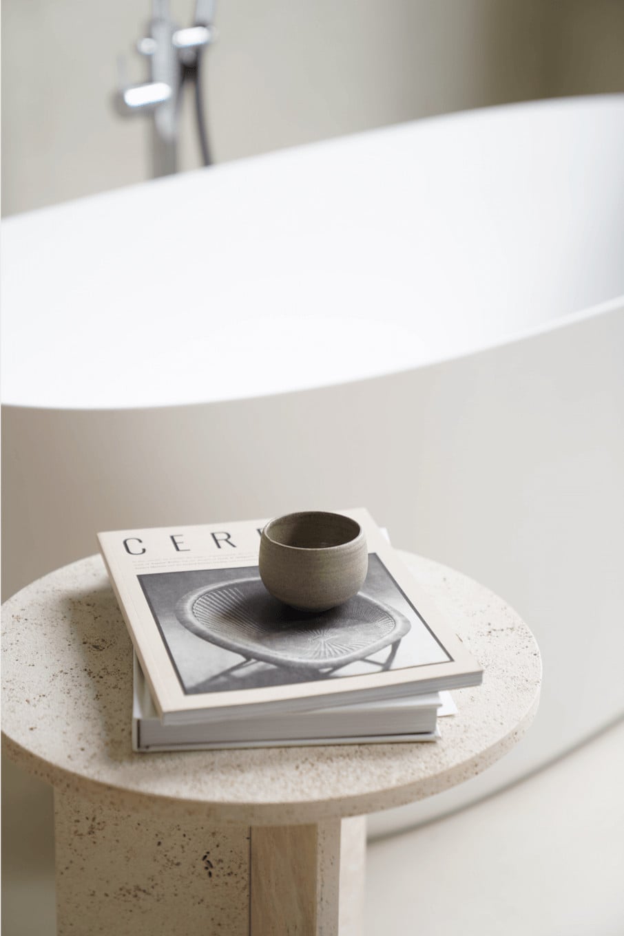 Hotel âme, Europe — Minimalist bathroom vanity with terrazzo table, ceramic vessel, design magazine, and soaking tub with chrome faucet in soft natural light.
