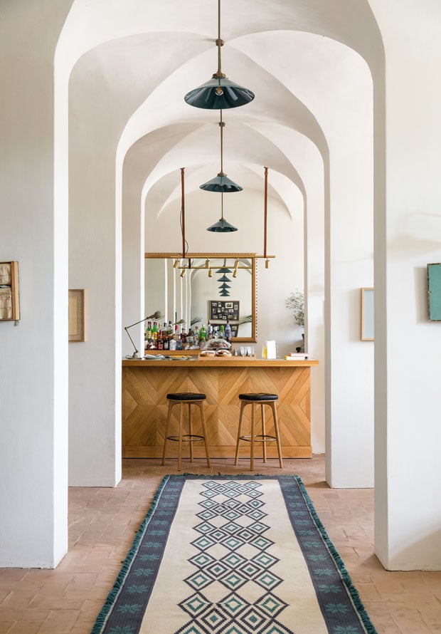 Hotel Bar, Europe — Barrel-vaulted corridor with pendant lights, wooden bar counter, terracotta floors, and geometric runner rug creating sophisticated minimalist hospitality design.