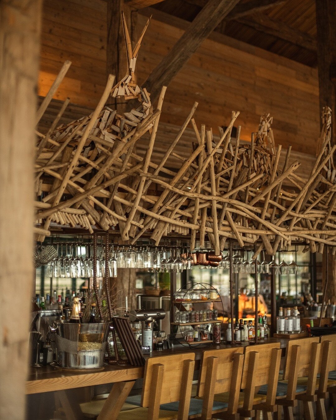Quinta da Comporta, Portugal — Rustic timber teepee installation above bar with woven branches, wooden chairs, and warm ambient lighting in luxury hospitality interior.