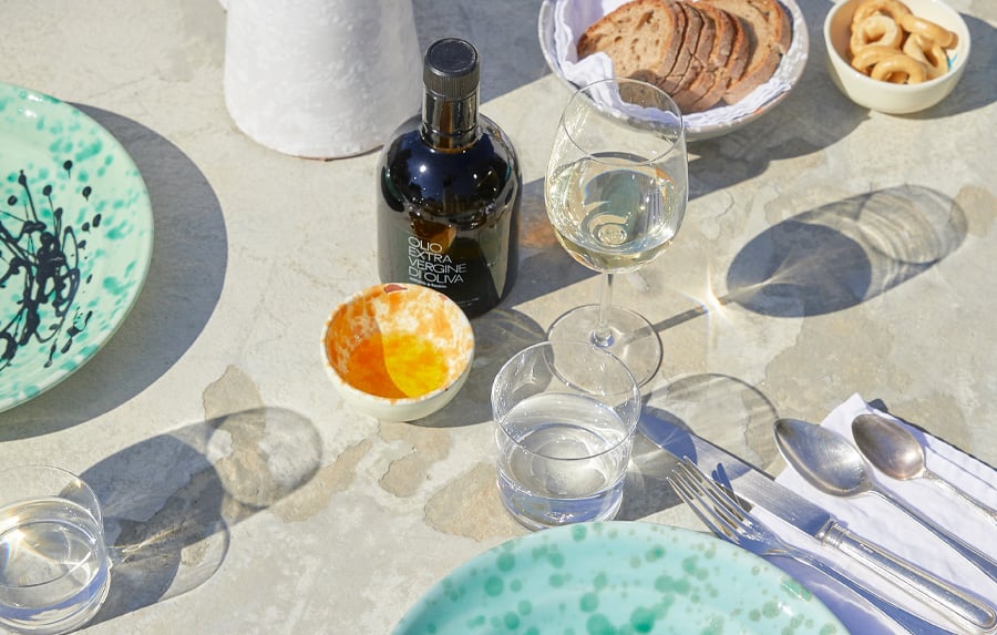 Masseria Moroseta, Europe — Outdoor table setting with turquoise ceramic plates, olive oil bottle, water glasses, bread and citrus fruit under Mediterranean sunlight.