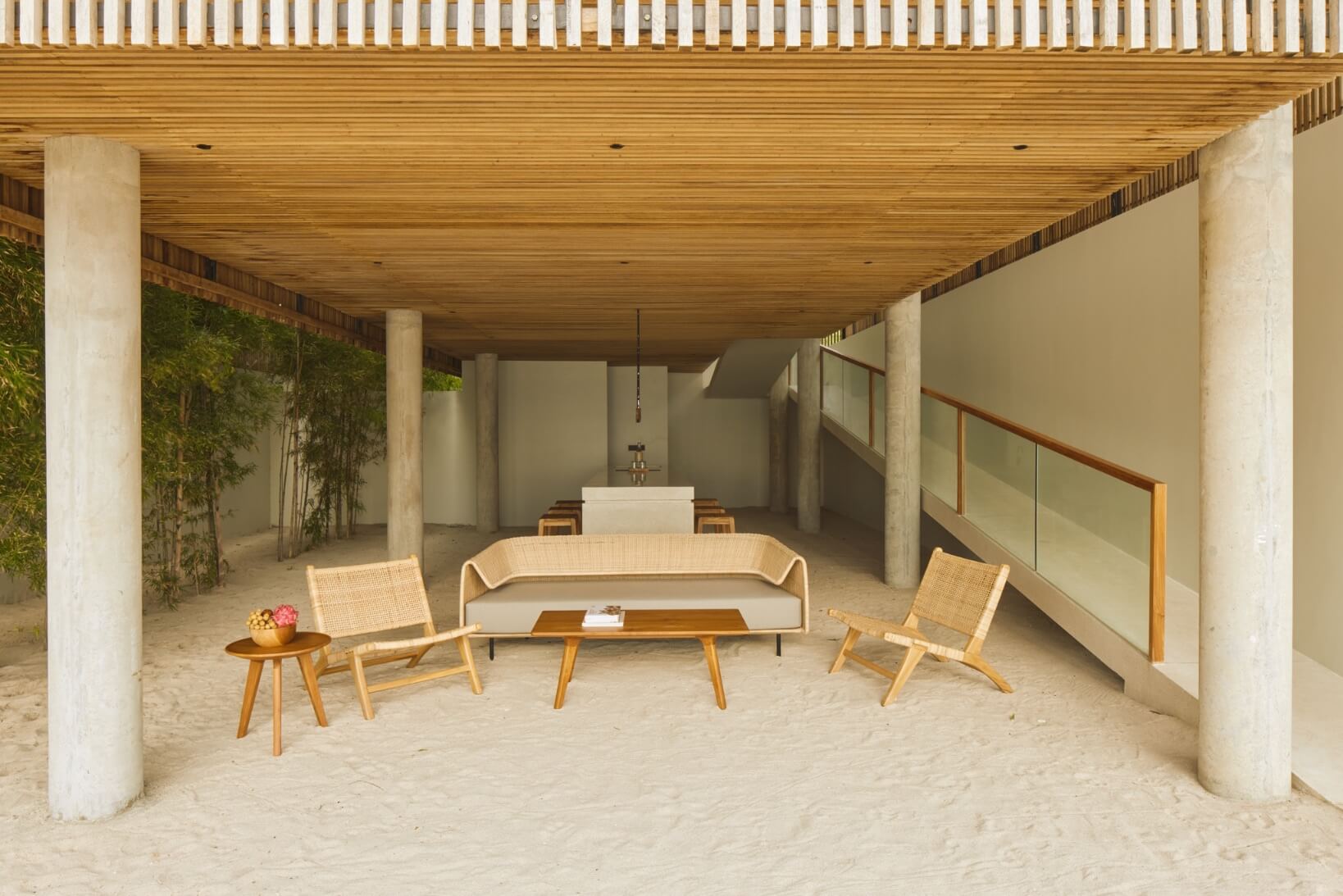 Innit Lombok, Asia — Covered sand terrace with mid-century modern furniture, concrete columns, wooden ceiling, and chapel altar visible in background.