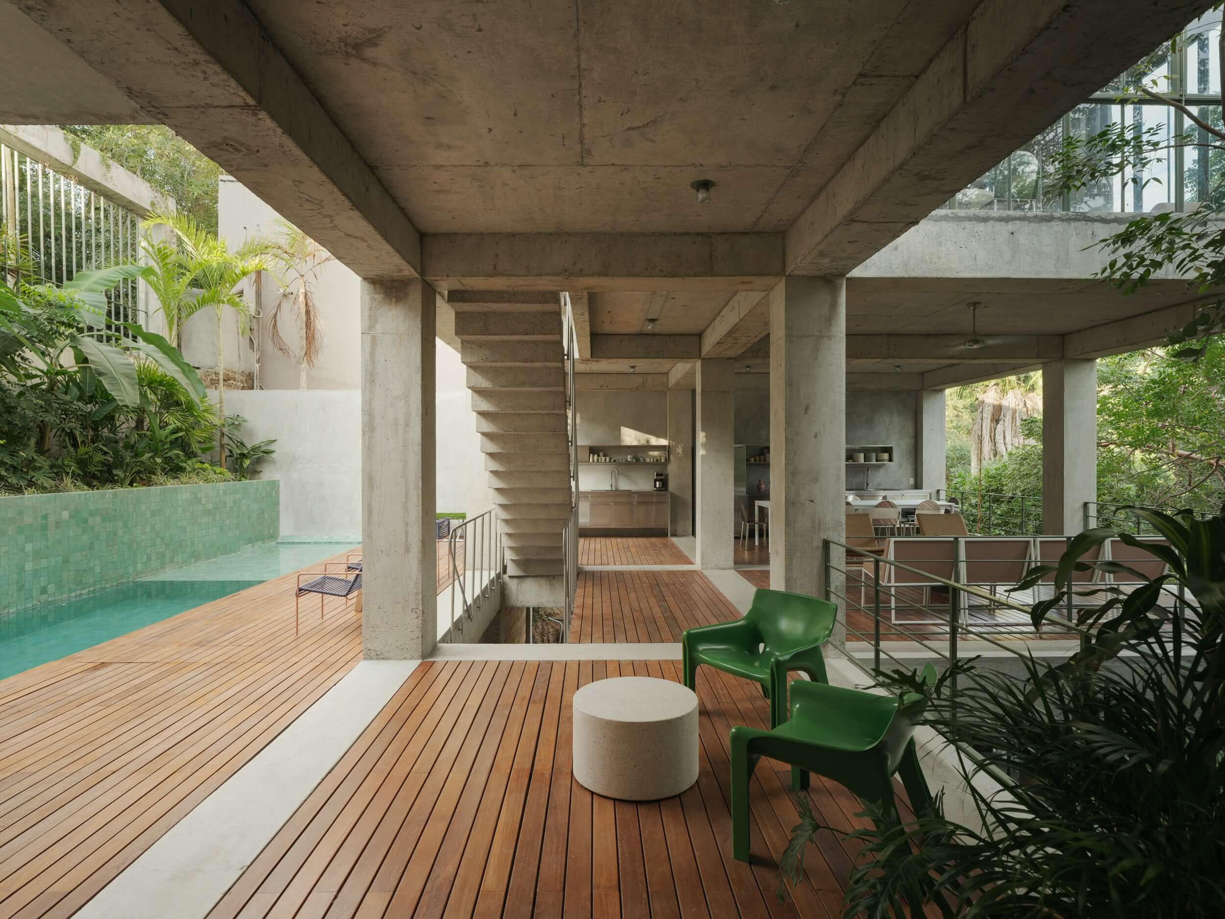 NICO, Mexico — Brutalist concrete terrace with teak decking, turquoise pool, green modern chairs, and lush vegetation under sculptural overhangs.