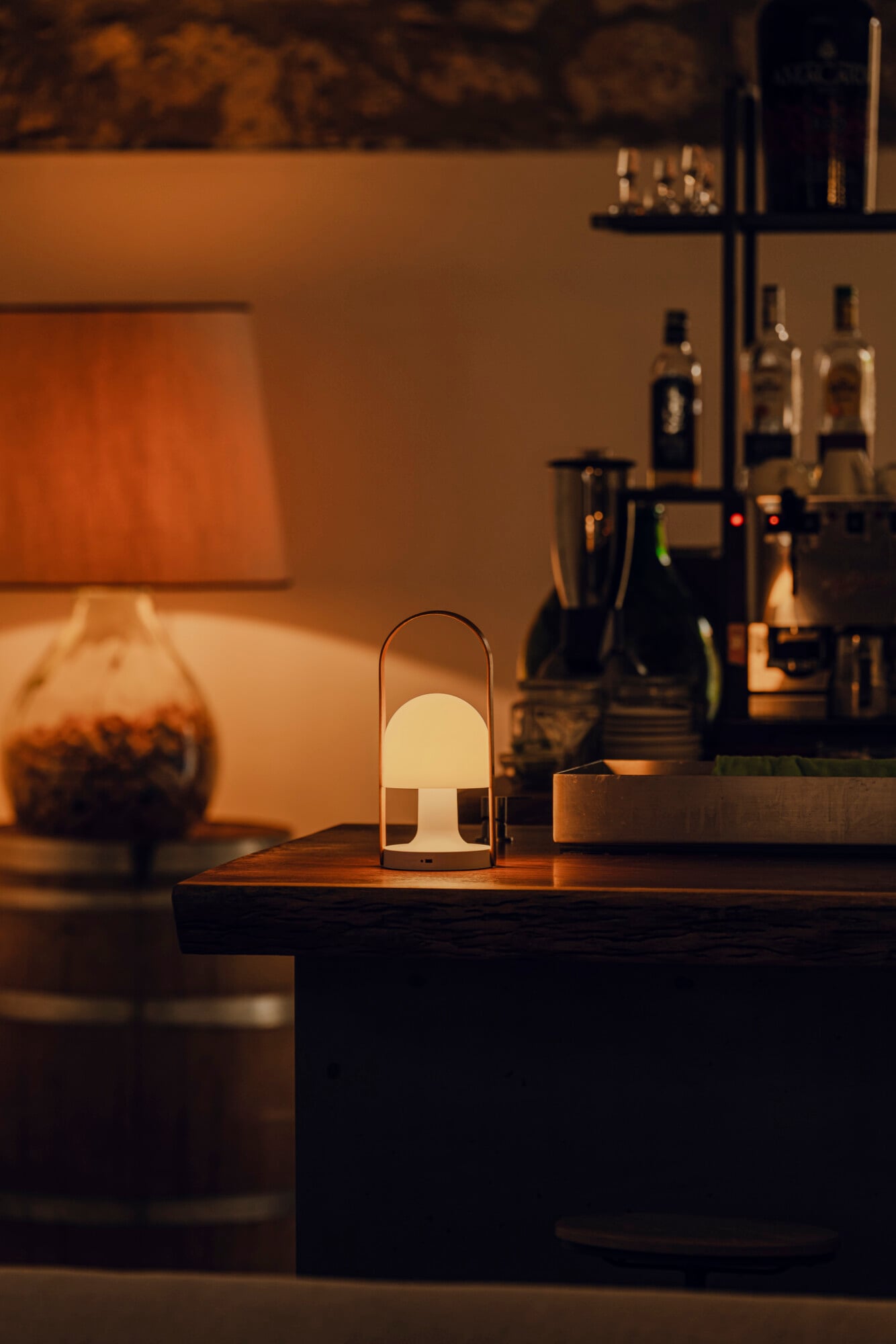 Susafa, Italy — Minimalist portable lamp with cream dome shade on dark wooden table, warm ambient lighting in luxury hospitality interior.