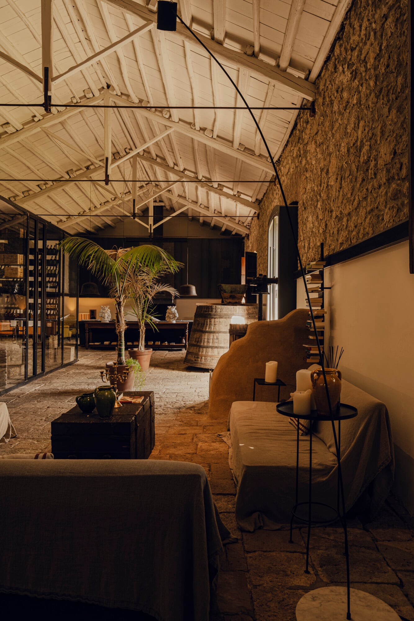Susafa, Italy — Barrel-vaulted brick interior with exposed wooden trusses, terracotta floors, potted palm, candlelit tables, and black metal furnishings creating warm hospitality ambiance.