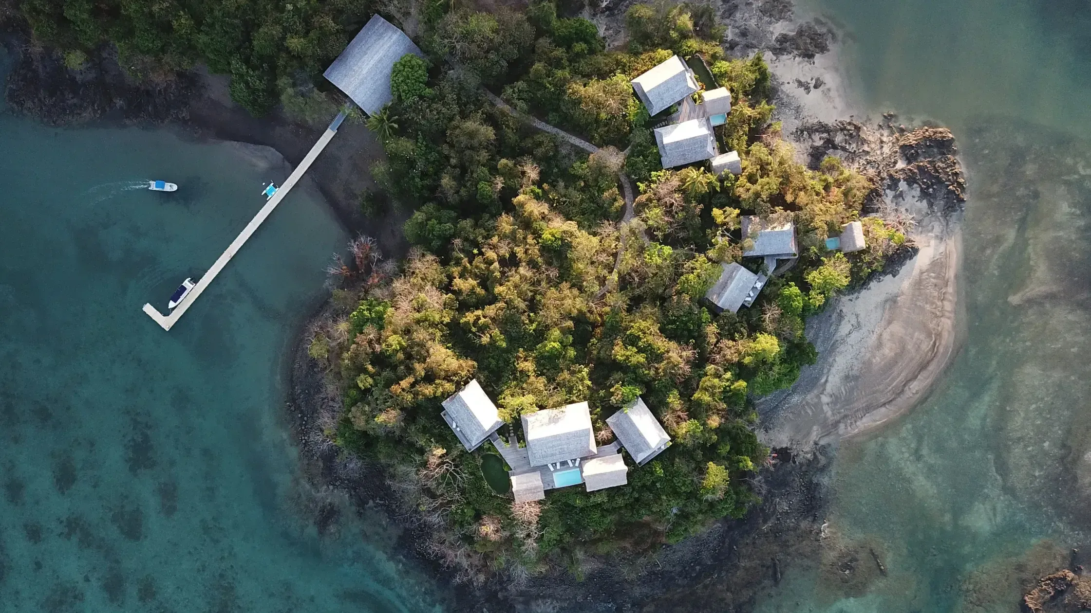 Islas Secas, Panama — Aerial view of luxury pavilions nestled in dense tropical forest overlooking turquoise waters with private dock and boats.