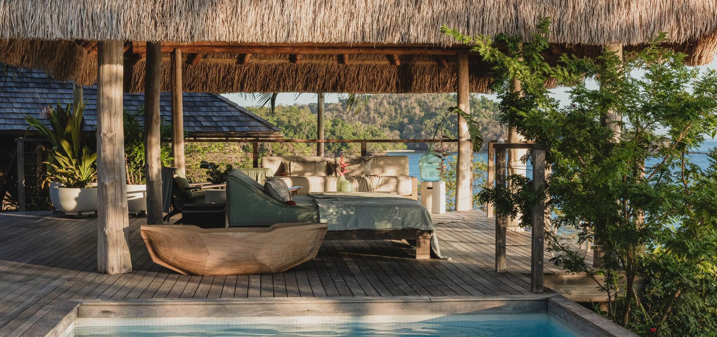 Islas Secas, Panama — Thatched-roof pavilion with wooden loungers overlooking ocean, infinity pool, and forested coastline at sunset.