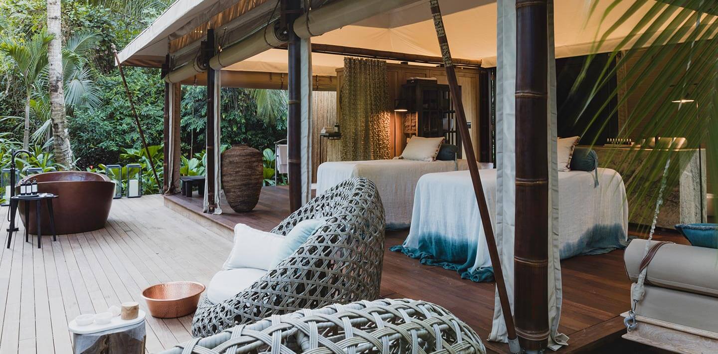 Secascent Spa — Open-air spa pavilions with woven loungers, canopied beds, wooden decking, tropical vegetation, and natural light filtering through palm fronds.