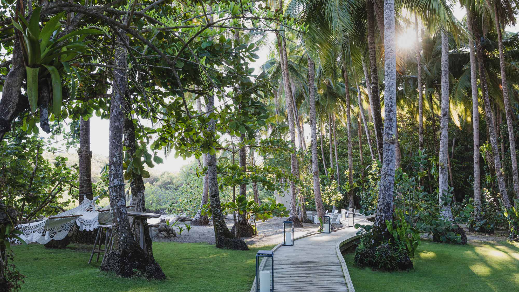 Islas Secas, Panama — Wooden boardwalk through palm grove with manicured lawn, hammock, and ocean view at sunset.