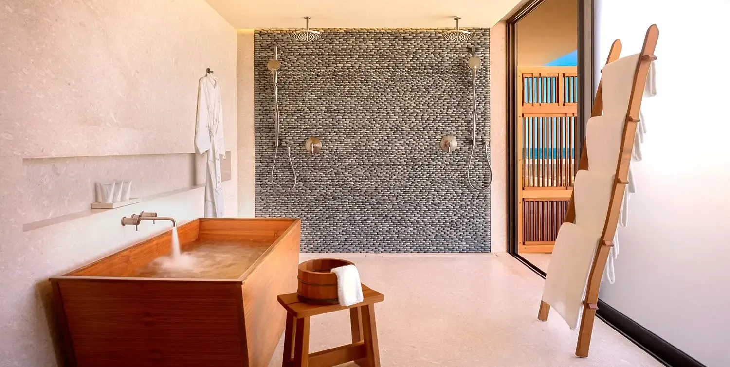 Nobu Los Cabos, Mexico — Japanese soaking tub and rainfall shower with mosaic tile wall in minimalist spa bathroom with natural light and wooden accents.