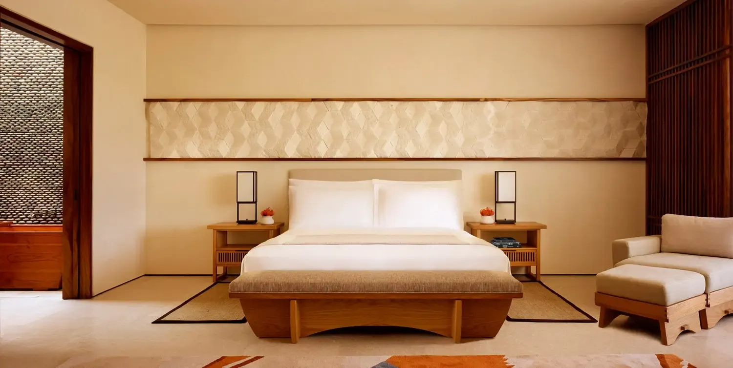 Nobu Los Cabos, Mexico — Minimalist bedroom with natural wood platform bed, cream bedding, geometric wall paneling, paired nightstands with brass lamps, and neutral palette emphasizing serene luxury design.