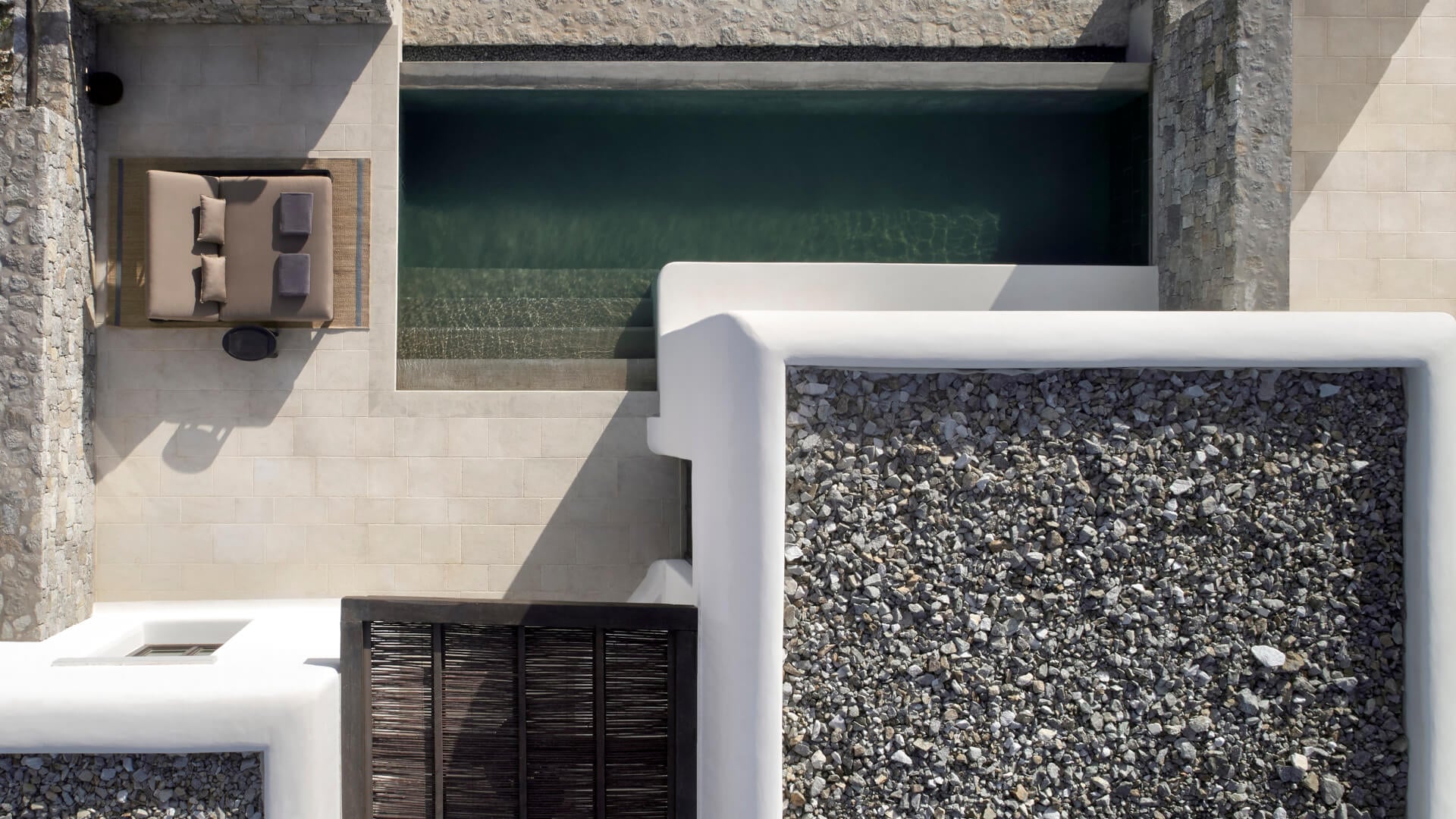 Kalesma, Europe — Minimalist courtyard with teal plunge pool, white stone walls, gravel beds, and modernist architectural details in natural sunlight.