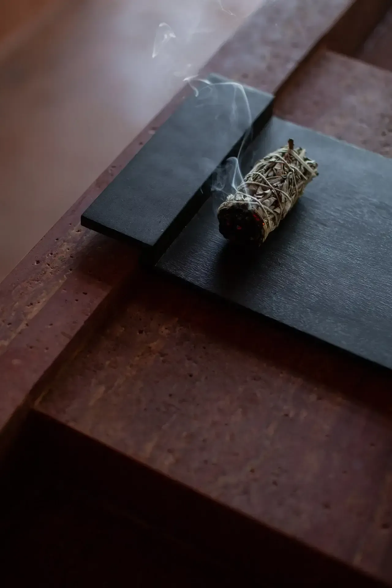 Further Hotel, Asia — Smoldering sage bundle on dark slate with wooden surface, minimalist wellness styling and moody atmospheric lighting