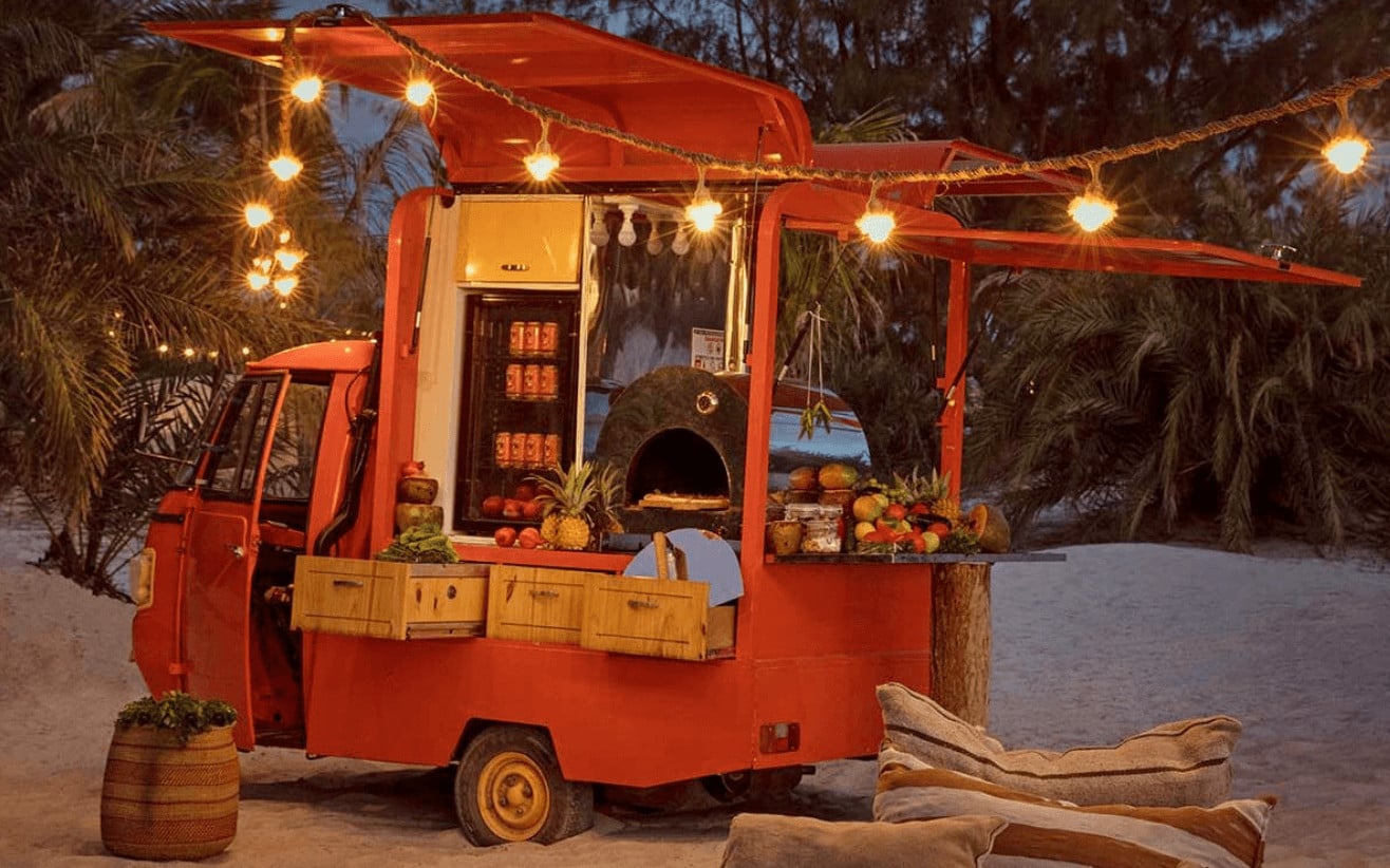 Pizza Tuk Tuk, Africa — Red converted truck with wood-fired oven, string lights, and tropical palms at dusk, beachside dining setup.