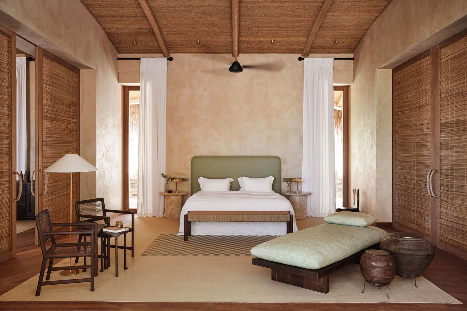Kisawa Sanctuary, Africa — Minimalist villa bedroom with sage headboard, woven wood doors, cream plaster walls, natural light, and sculptural furnishings.