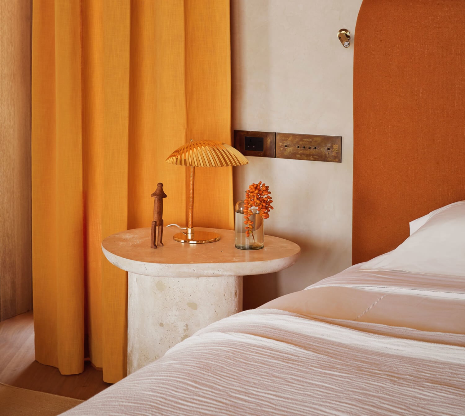 Kisawa Sanctuary, Africa — Minimalist bedroom with warm terracotta walls, pleated brass lamp, travertine side table, and flowing linen bedding in natural light.