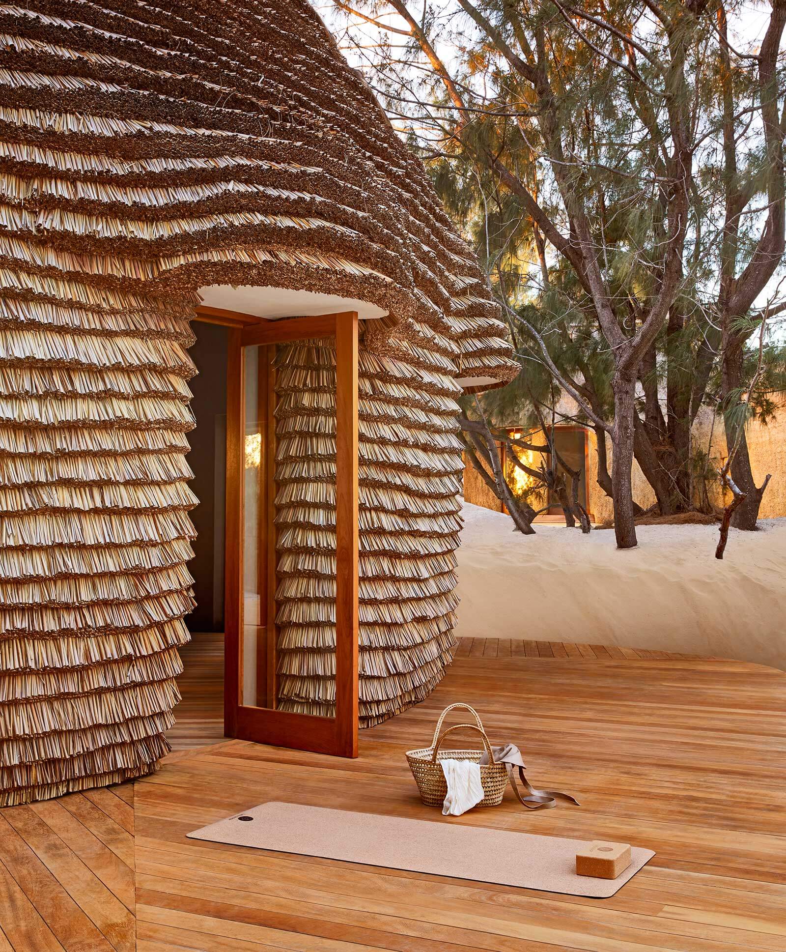 Yoga Nest, Africa — Woven thatch pavilion with timber deck, open doorway, and yoga mat overlooking eucalyptus trees in serene desert landscape.