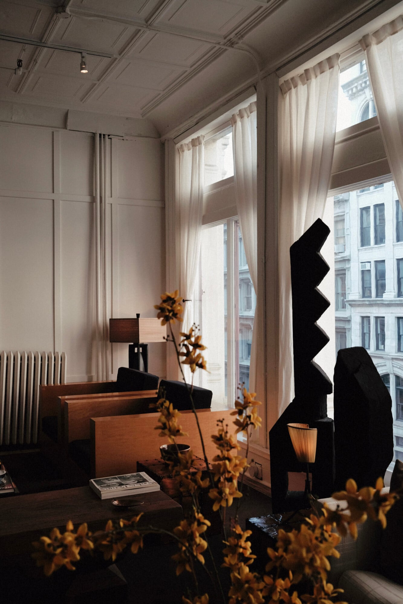 Spencer's: Wellness by Design — Minimalist office with natural light, wooden desk, black sculptural furniture, dried botanicals, and city views through floor-to-ceiling windows.