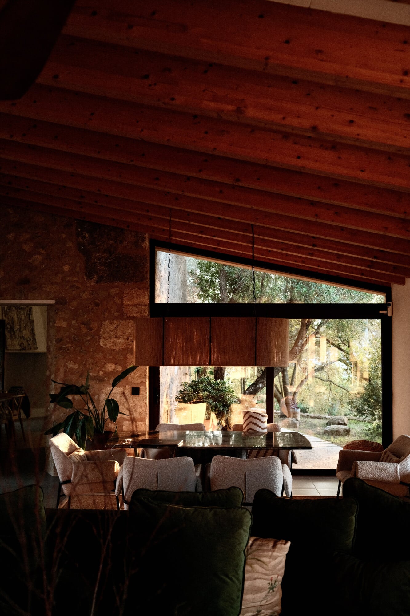 Vista Verde, Balearic Islands — Dining room with exposed wood beams, terracotta walls, and floor-to-ceiling windows opening onto Mediterranean garden courtyard.