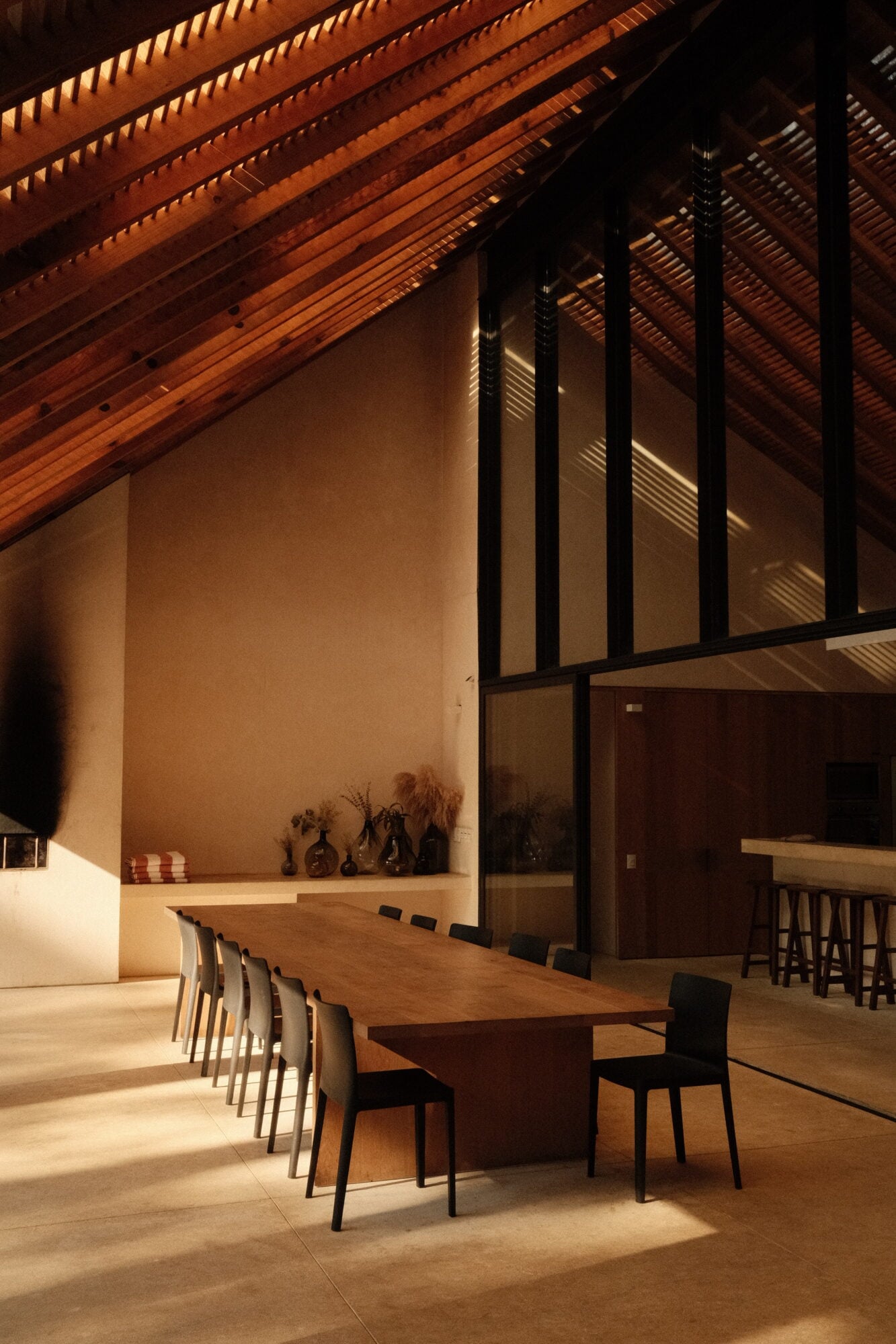 Casa Zarzales, Mexico — Wooden dining table with black chairs beneath soaring timber ceiling and clerestory windows casting warm light across minimalist interior.