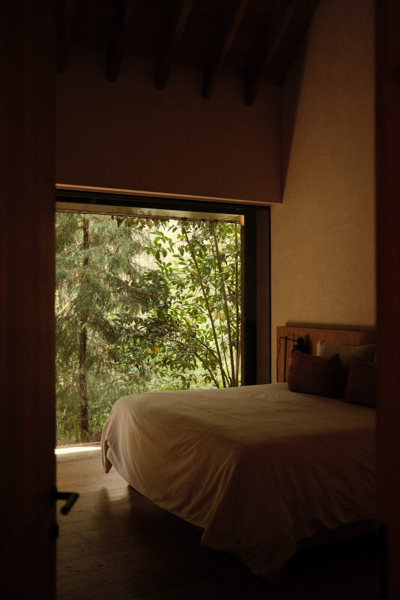 Minimalist bedroom at Casa Zarzales with white linens overlooking lush green vegetation through floor-to-ceiling glass doors.