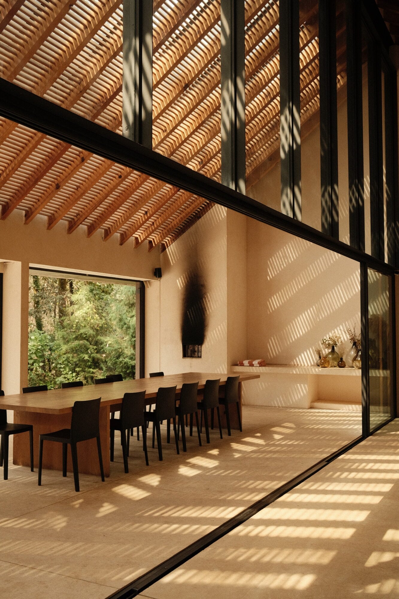 Minimalist dining room at Casa Zarzales with wooden pergola, natural light patterns, and forest views through expansive glazing.