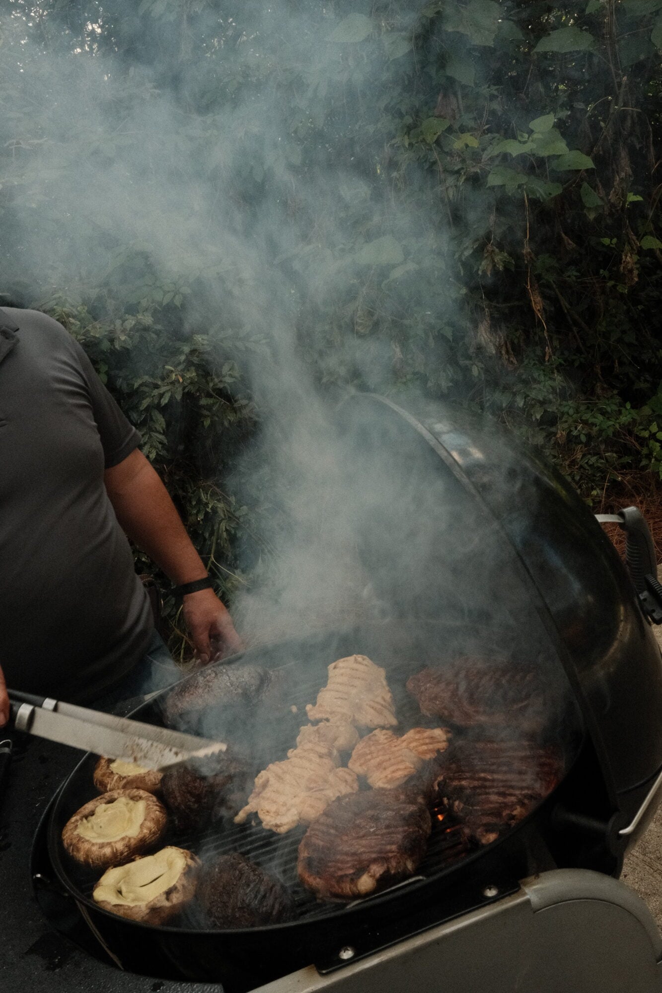 Casa Zarzales, Mexico — Chef grilling meat and mushrooms over open flame with billowing smoke in lush jungle garden setting.