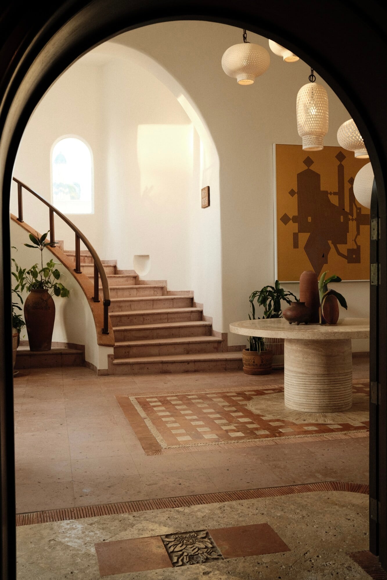 Maroma, A Belmond Hotel, Mexico — Arched entryway to travertine courtyard with perforated pendant lights, terracotta stairs, potted plants, and geometric tile patterns.