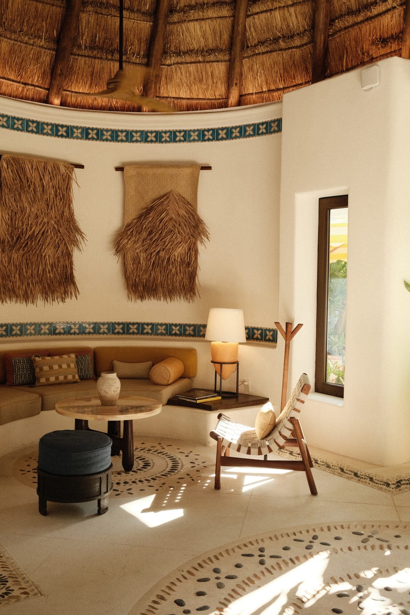 Maroma, A Belmond Hotel, Mexico — Circular thatched-roof lounge with cream walls, woven wall hangings, geometric trim, wooden furniture, and patterned floor in warm earth tones.