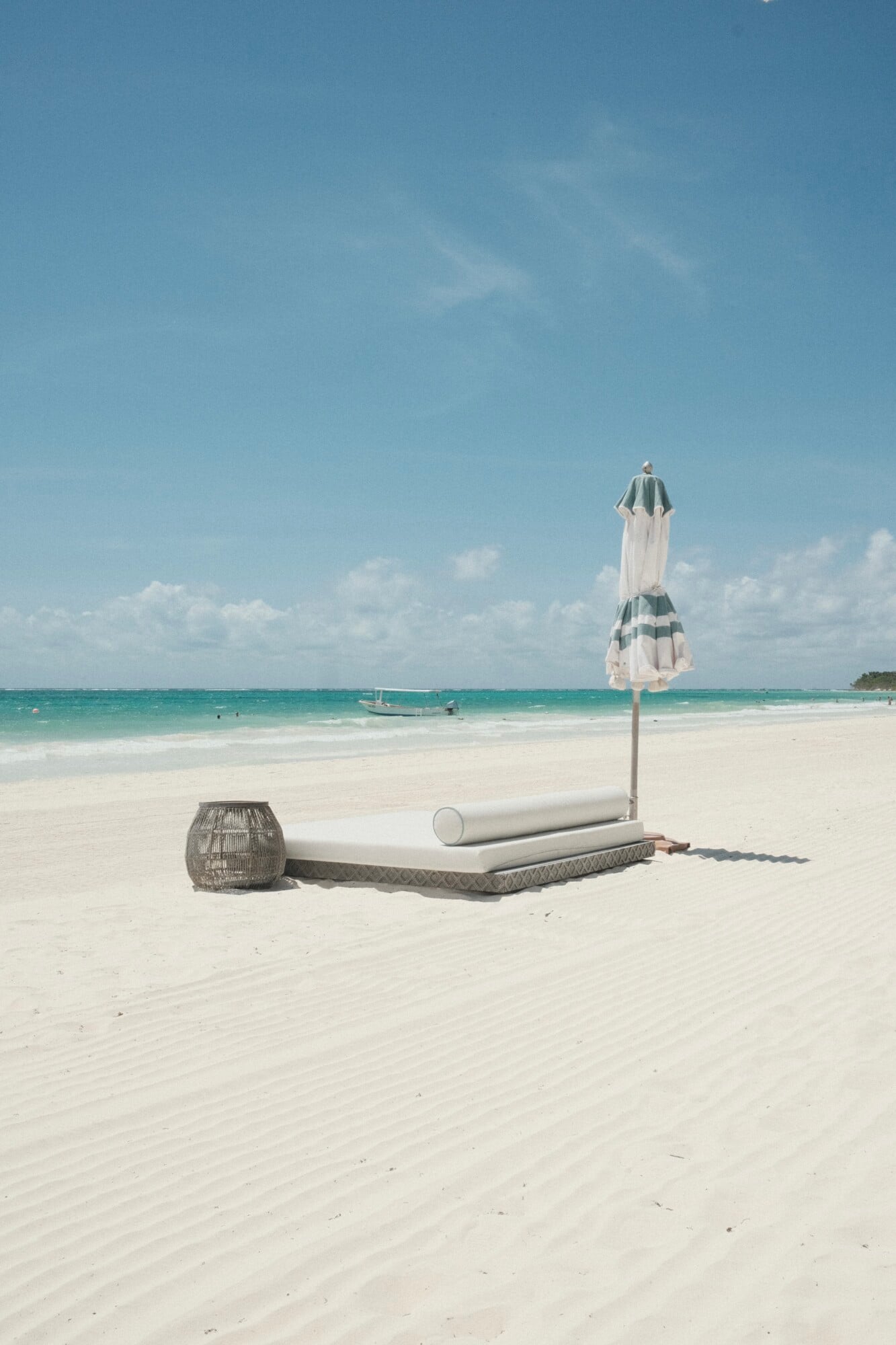 Maroma, A Belmond Hotel, Mexico — Striped beach umbrella and woven seating on white sand with turquoise Caribbean waters and traditional fishing boat.