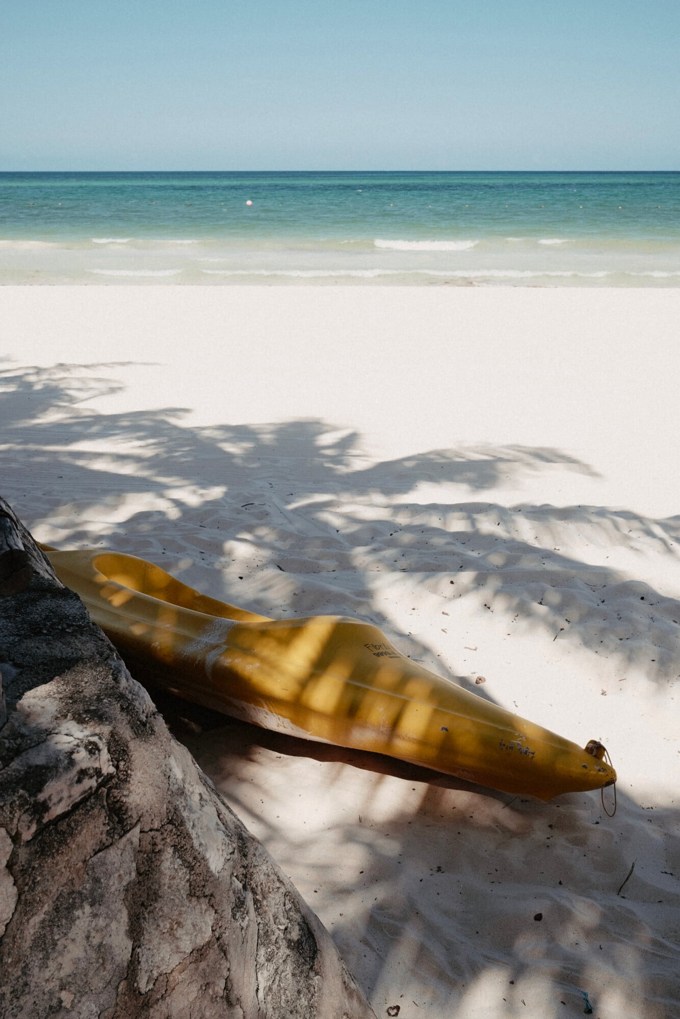 Maroma, A Belmond Hotel, Mexico — Yellow kayak resting on white sand beach with dappled tree shadow, turquoise ocean and horizon beyond.