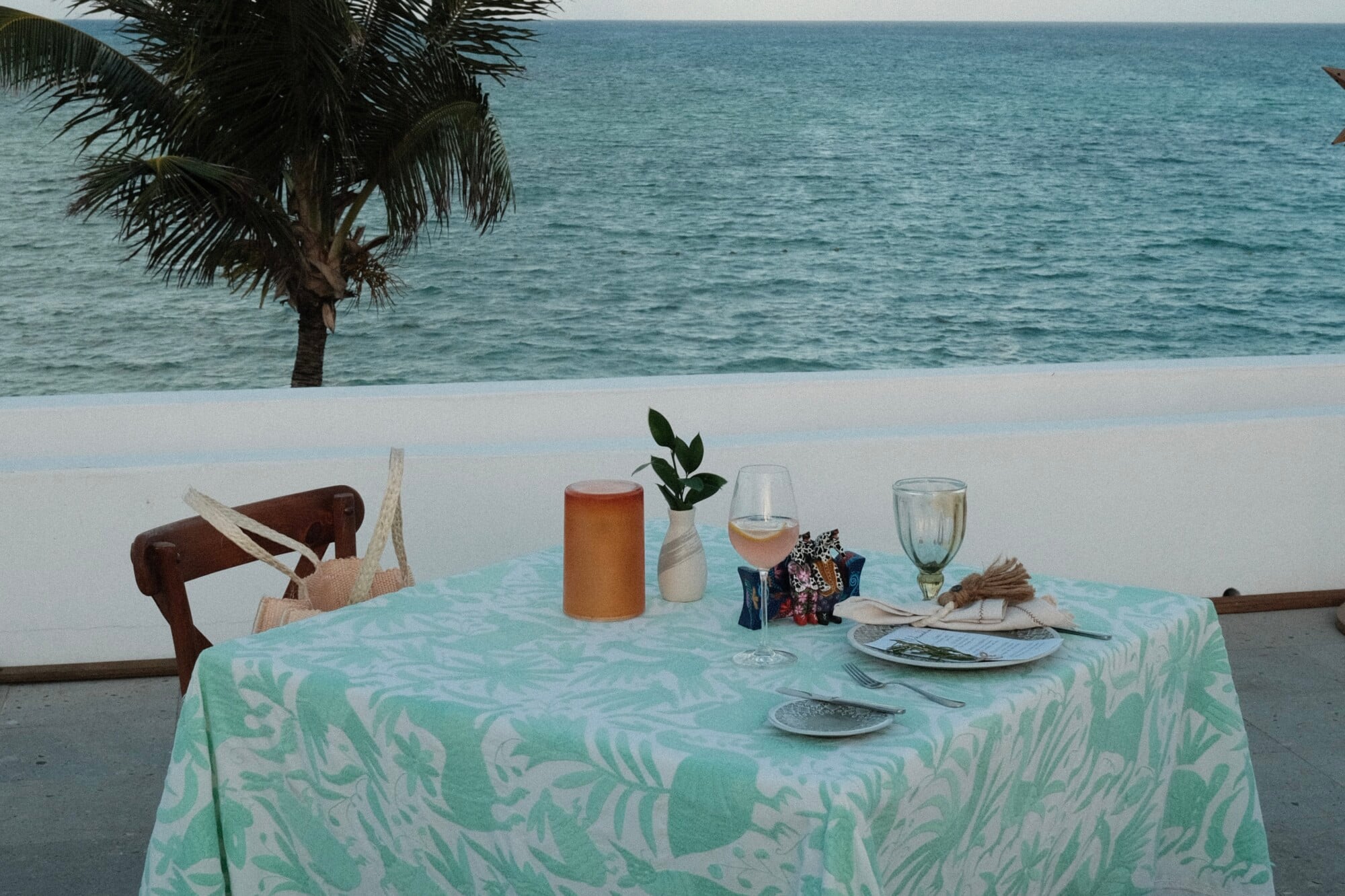 Pink-Nic Dinner, Mexico — Beachfront table with mint patterned linen, place settings, rosé wine, and palm tree overlooking turquoise sea.