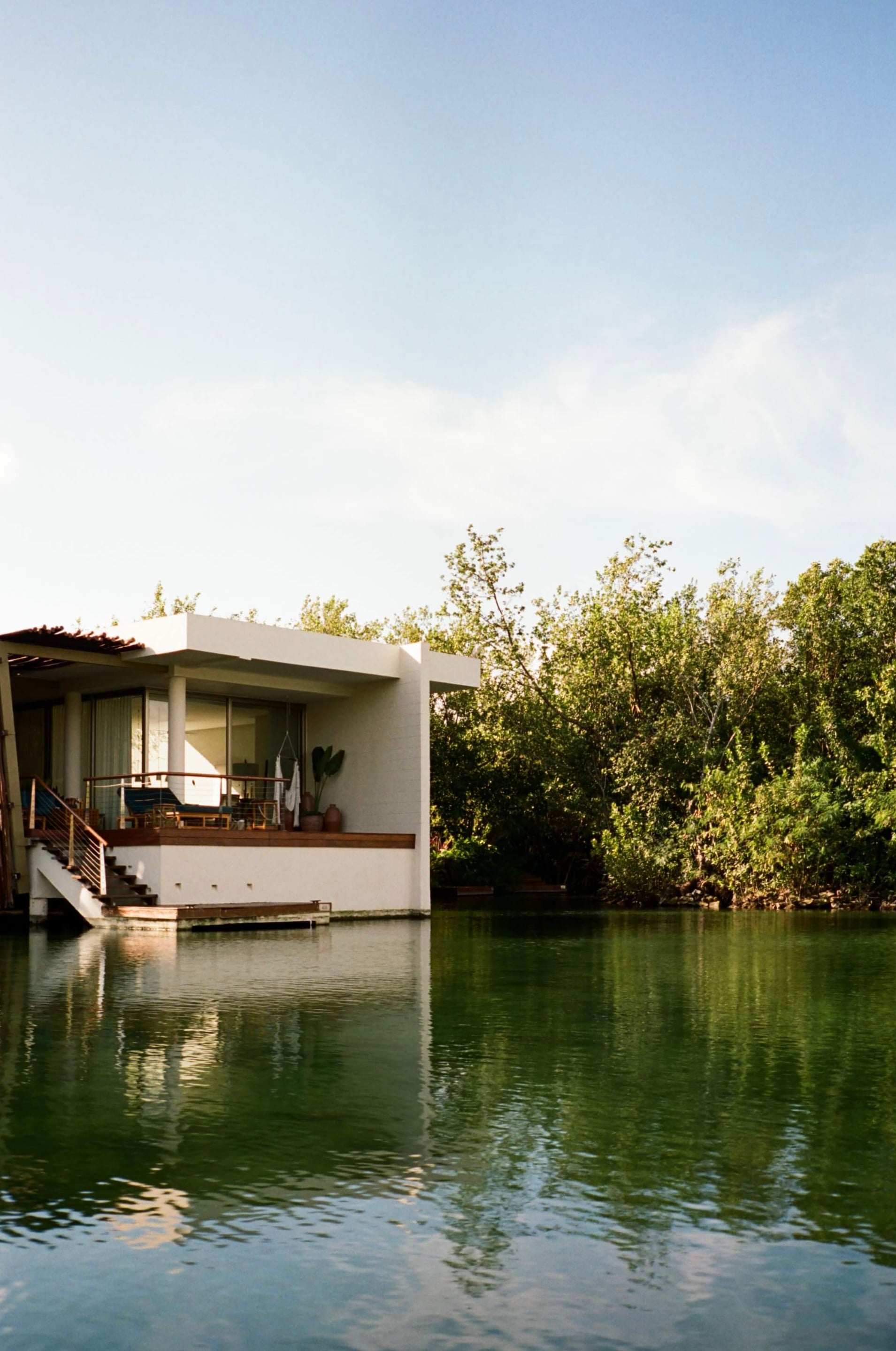 Rosewood Mayakoba, Mexico — Minimalist waterfront pavilion with white concrete, wooden deck, and floor-to-ceiling glass overlooking mangrove lagoon at sunset.