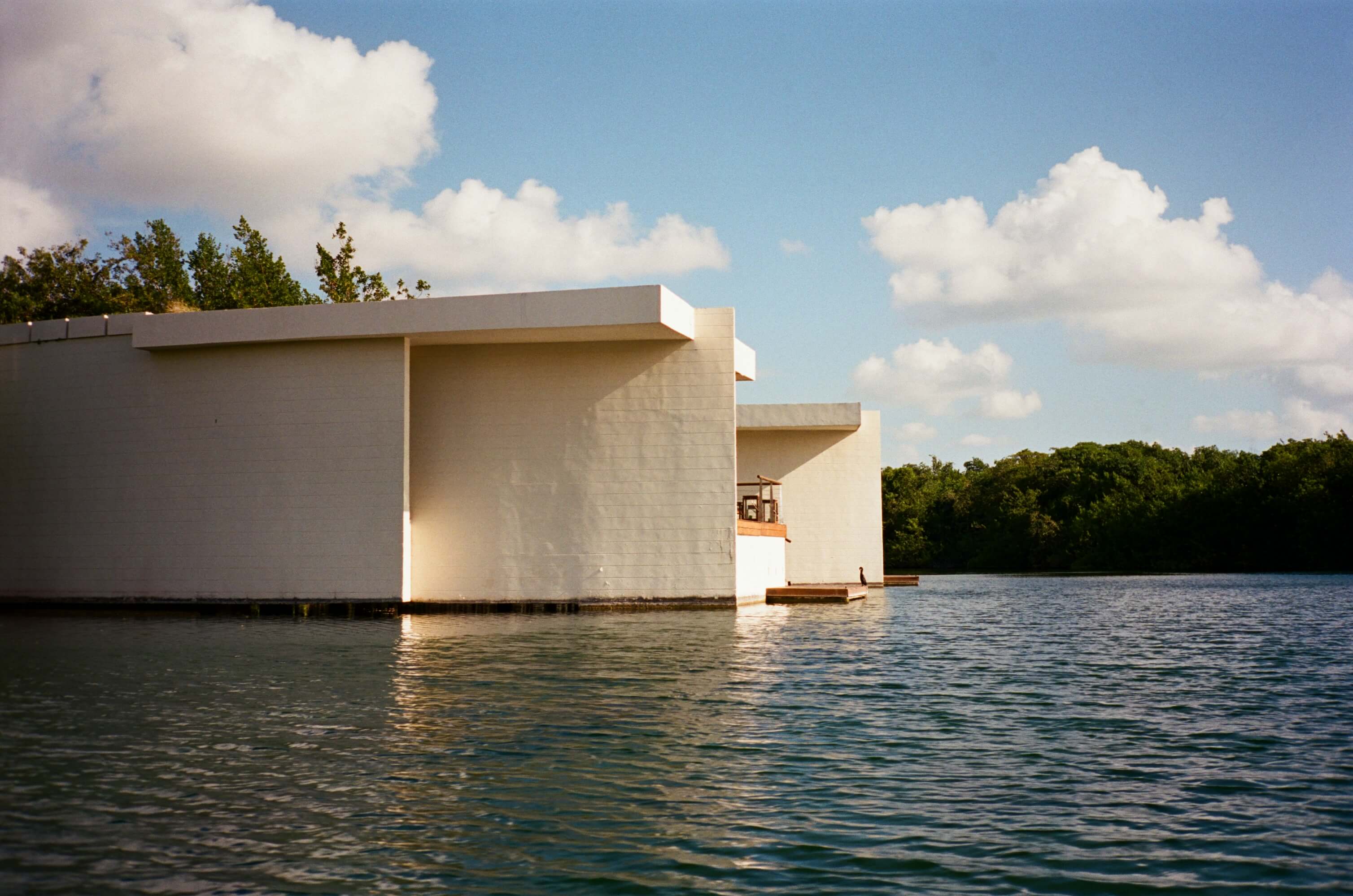 Rosewood Mayakoba, Mexico — Modernist waterfront pavilion with geometric white concrete forms overlooking lagoon and mangrove forest under clear sky.