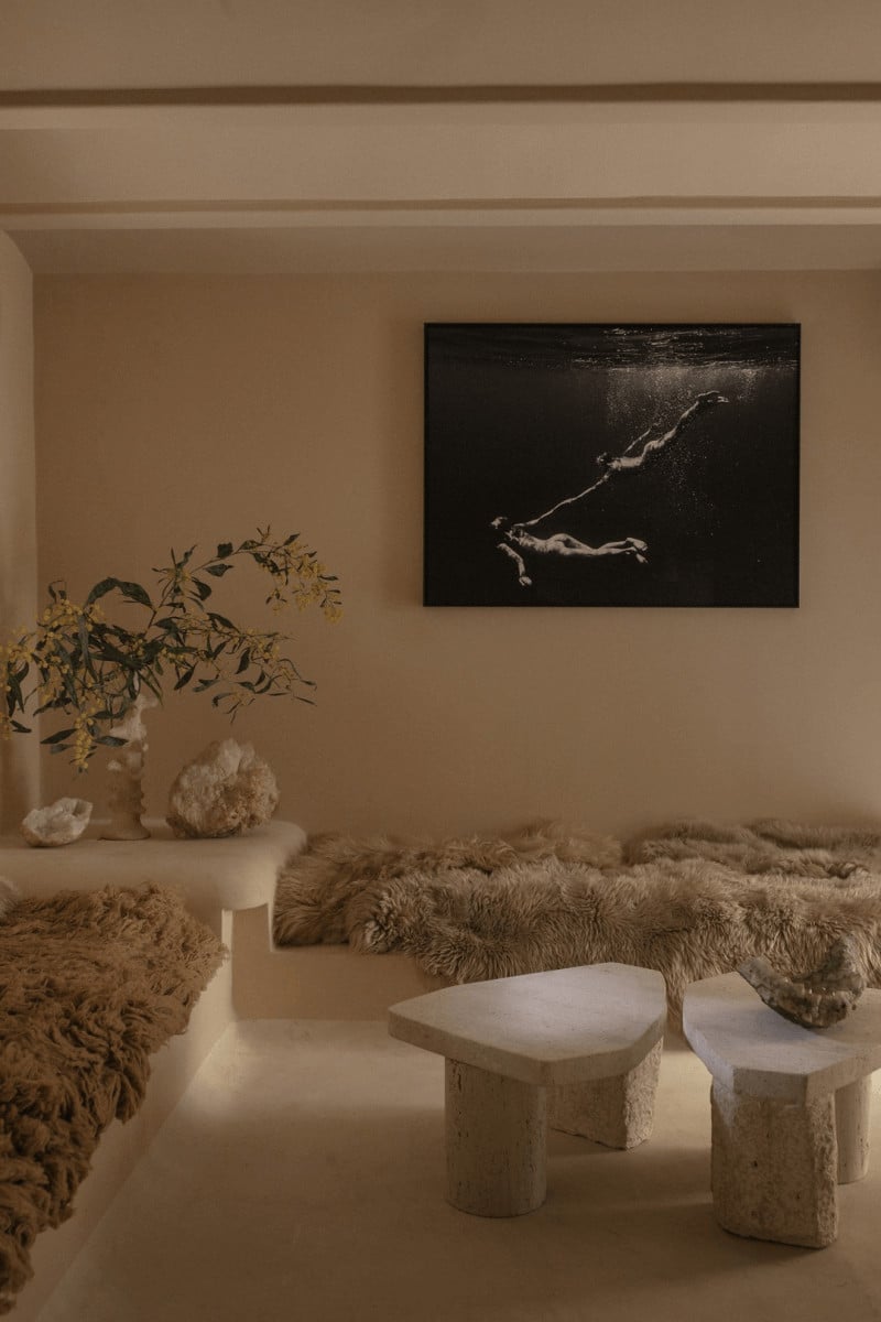 Hotel Corazón, Balearic Islands, Spain — Minimalist bedroom with travertine sculptural stools, dried botanicals, textured rugs, and black and white underwater photography on neutral walls.
