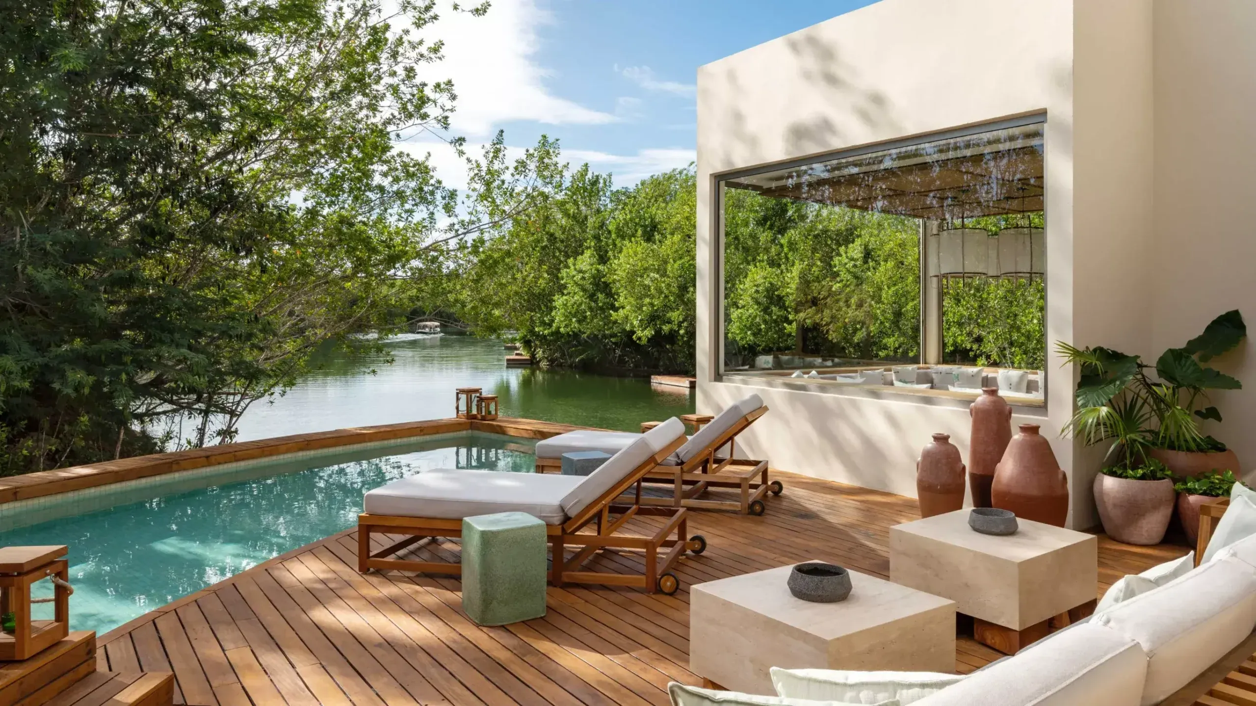 Rosewood Mayakoba, Mexico — Waterfront deck with teak loungers, turquoise pool, modern pavilion, mangrove views, and minimalist stone planters at sunset.