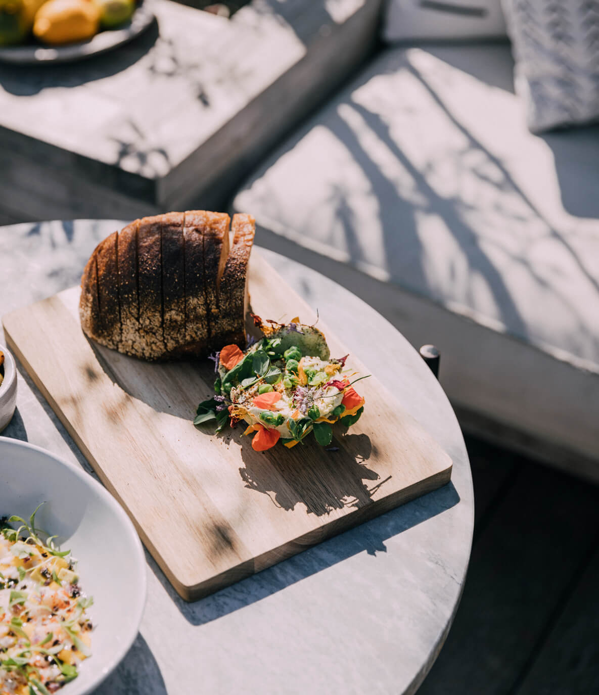 The Surfrider, North America — Plated charcuterie with scored duck breast, microgreens and edible flowers on marble table in sunlight.