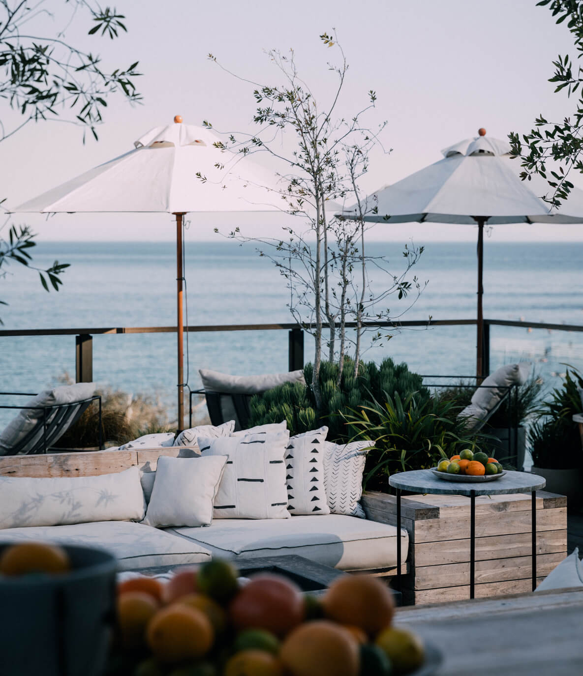 Roof Deck Bar, North America — Coastal terrace with white umbrellas, lounge seating, fresh citrus, and calm sea view at dusk.