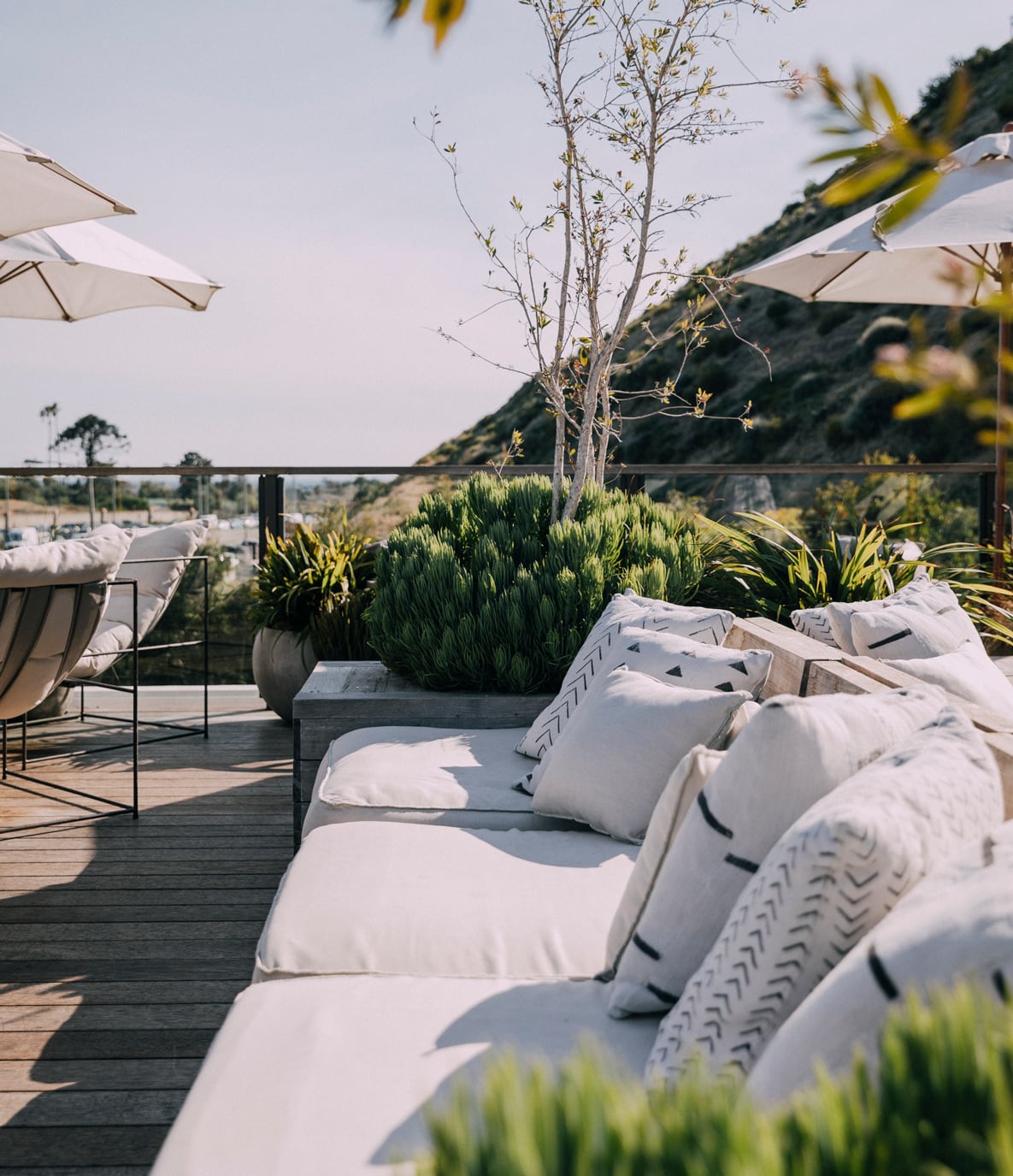 The Surfrider, North America — Coastal terrace with white loungers, linen pillows, potted greenery, and hillside views at dusk.