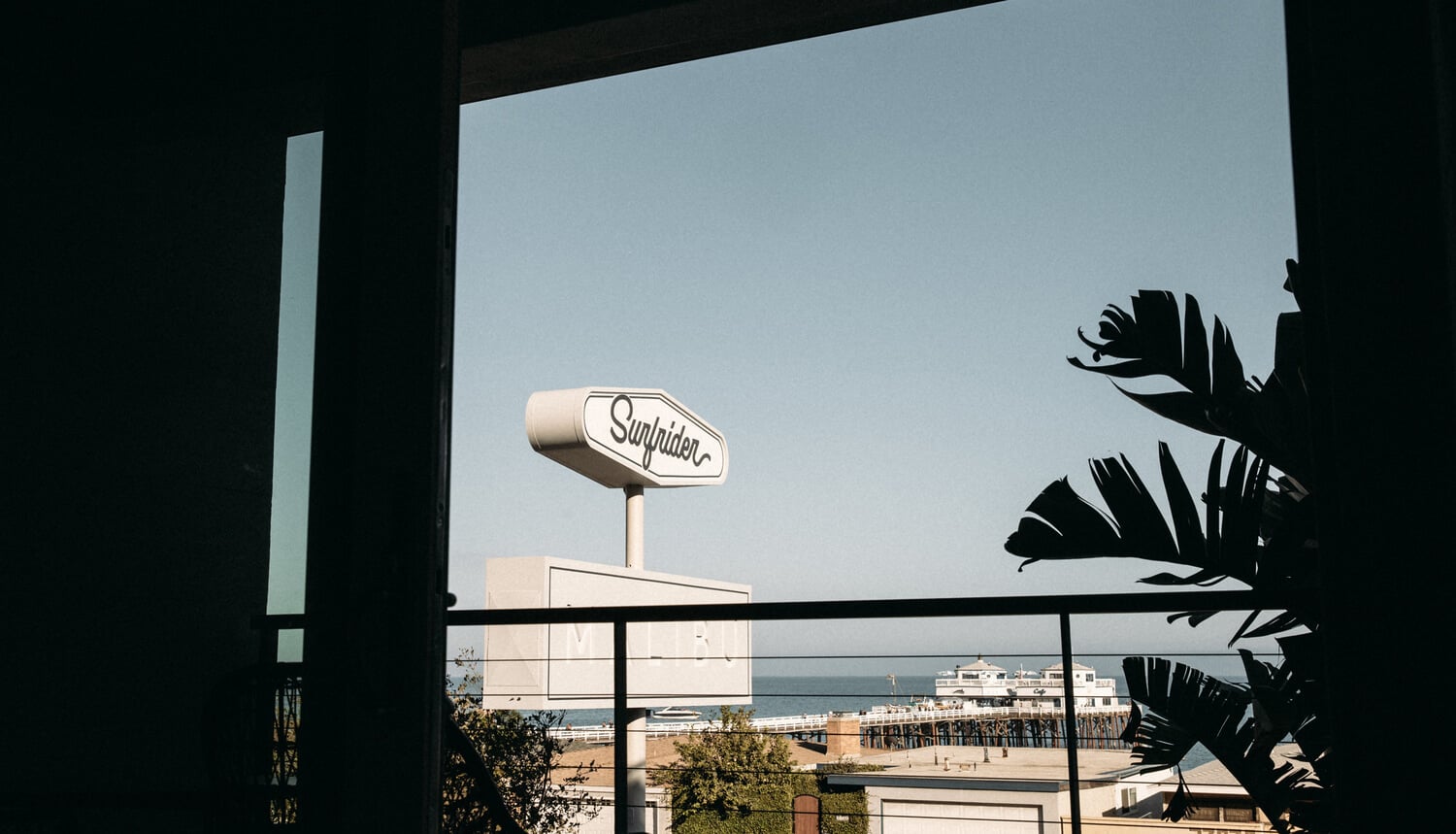 The Surfrider, North America — Surfrider sign overlooking beach and pier from modernist balcony with palm fronds and ocean view.