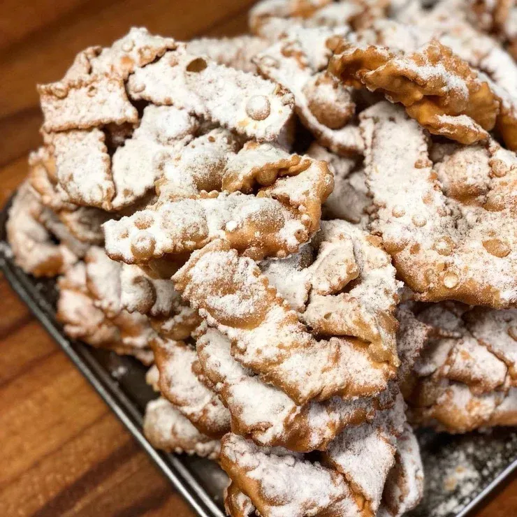 Pasticceria Tacconi — Powdered sugar-dusted pastries stacked on dark plate, Italian bakery confections with crispy, textured surfaces and warm golden-brown tones.