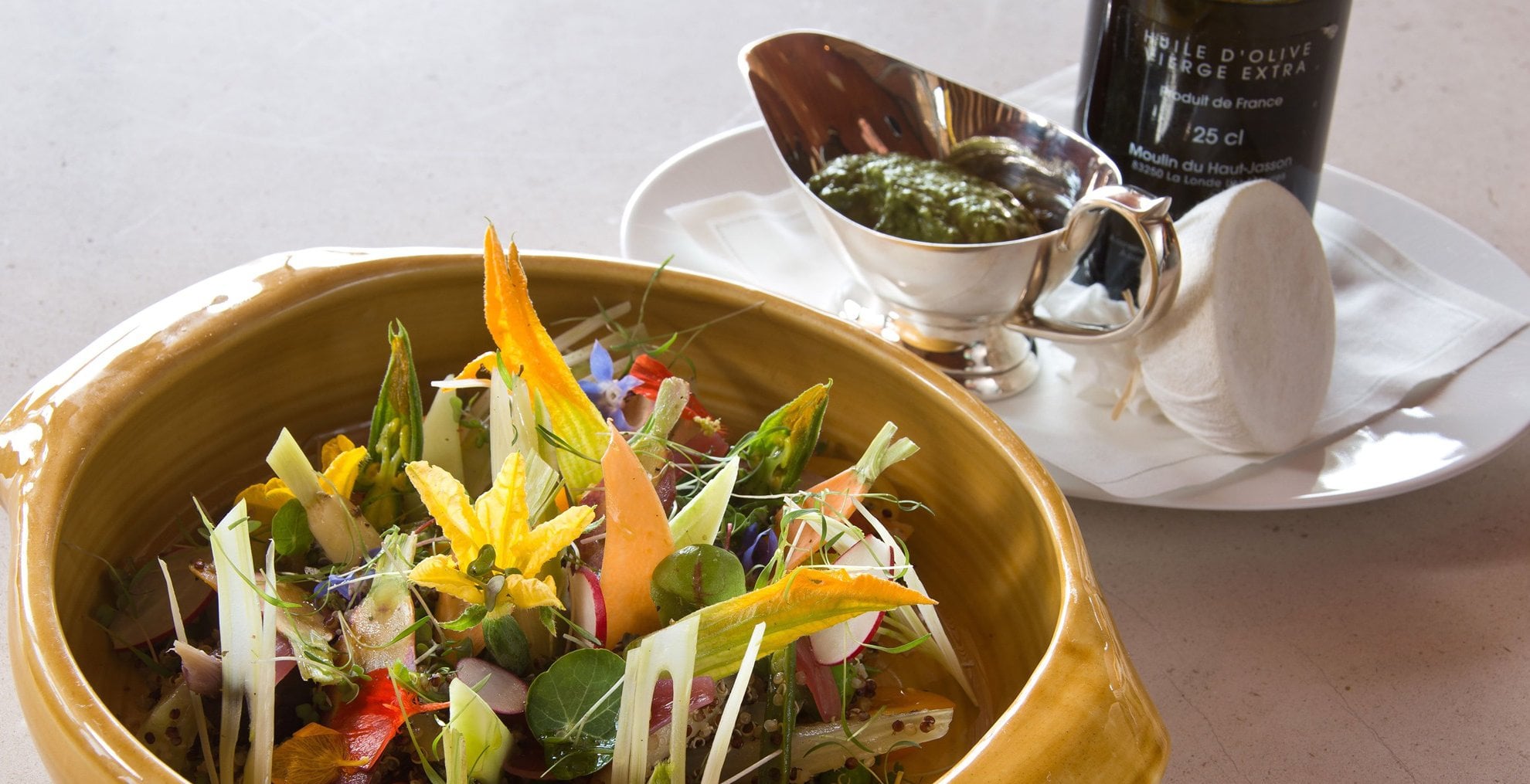 Pépé, Europe — Artfully plated salad with edible flowers and microgreens in golden bowl, French olive oil bottle and herb condiment alongside, fine dining presentation.