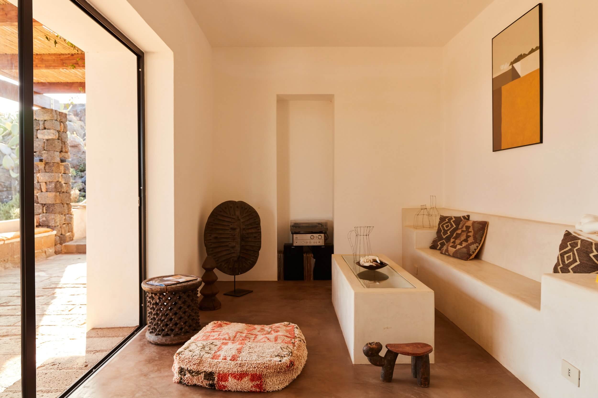 Parco Dei Sesi, Europe — Minimalist gallery space with cream walls, wooden floors, African masks, woven textiles, and sculptural furnishings bathed in natural light.