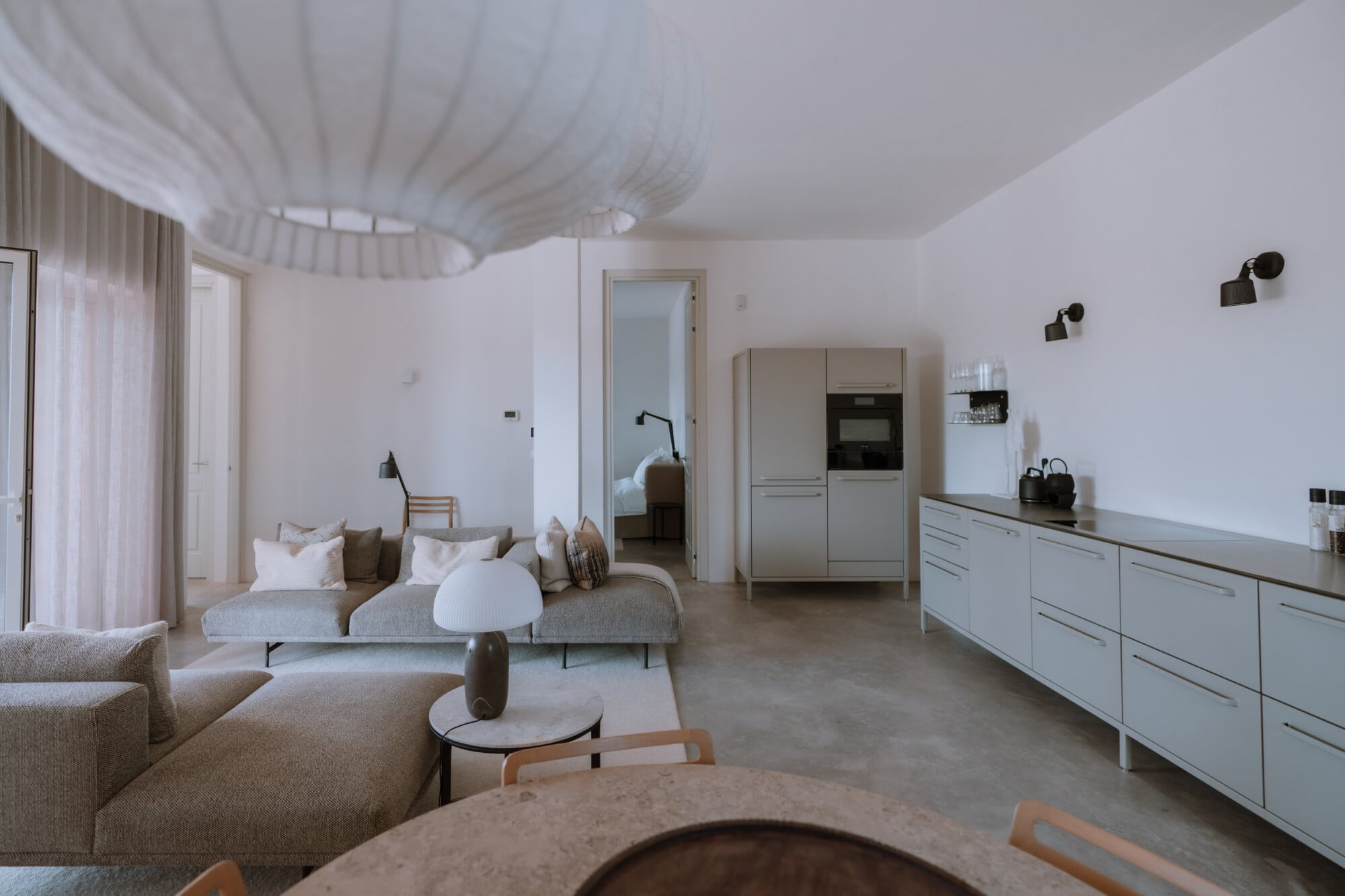 Villa Quercia, Italy — Open-plan living space with sculptural furniture, curved ceiling detail, neutral palette, and seamless kitchen integration flooded with natural light.